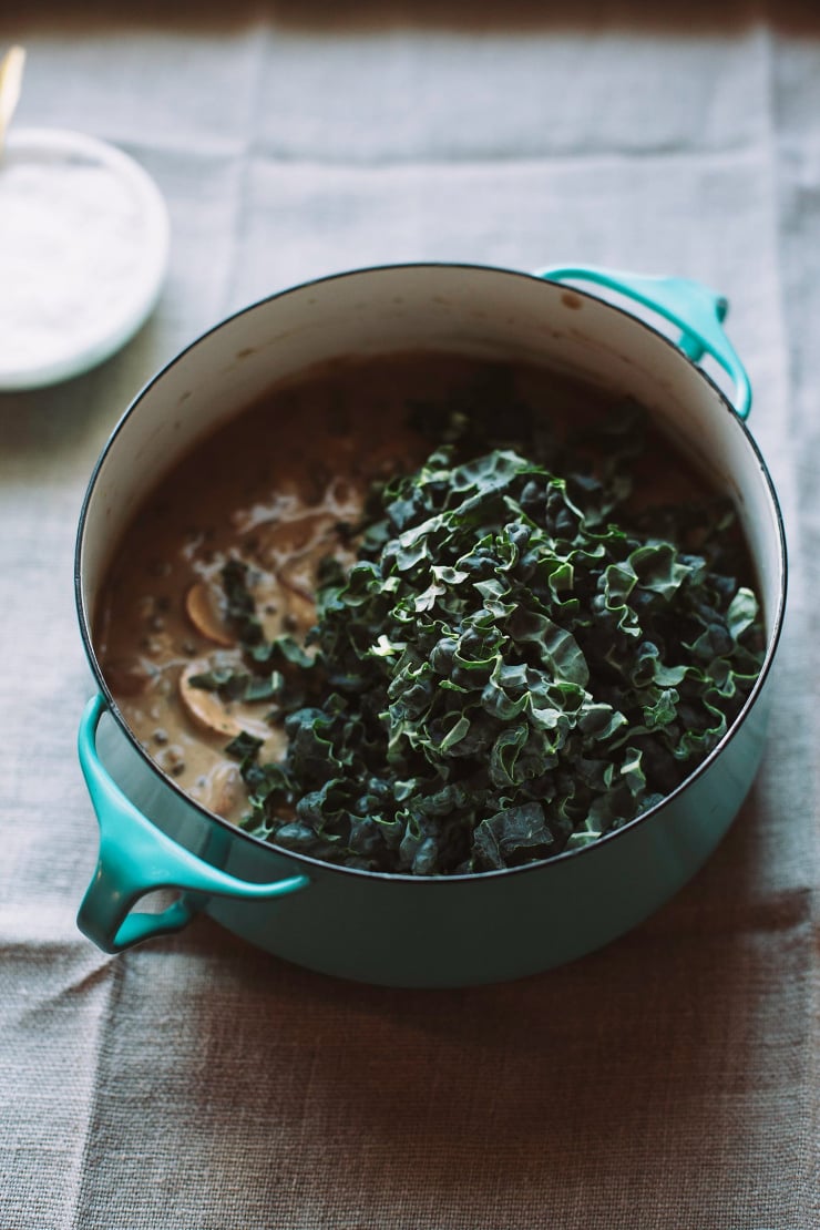 A 3/4 angle shot of a mushroom stew with a pile of ribboned kale added to the top.