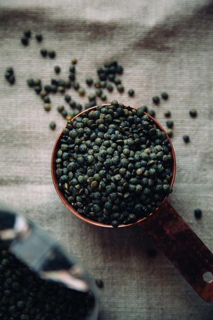 Overhead shot of dry French lentils in a copper measuring cup
