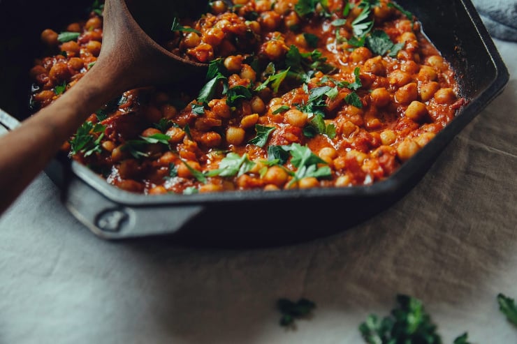 A 3/4 angle shot of seven spice chickpea stew in a cast iron skillet topped with chopped parsley.