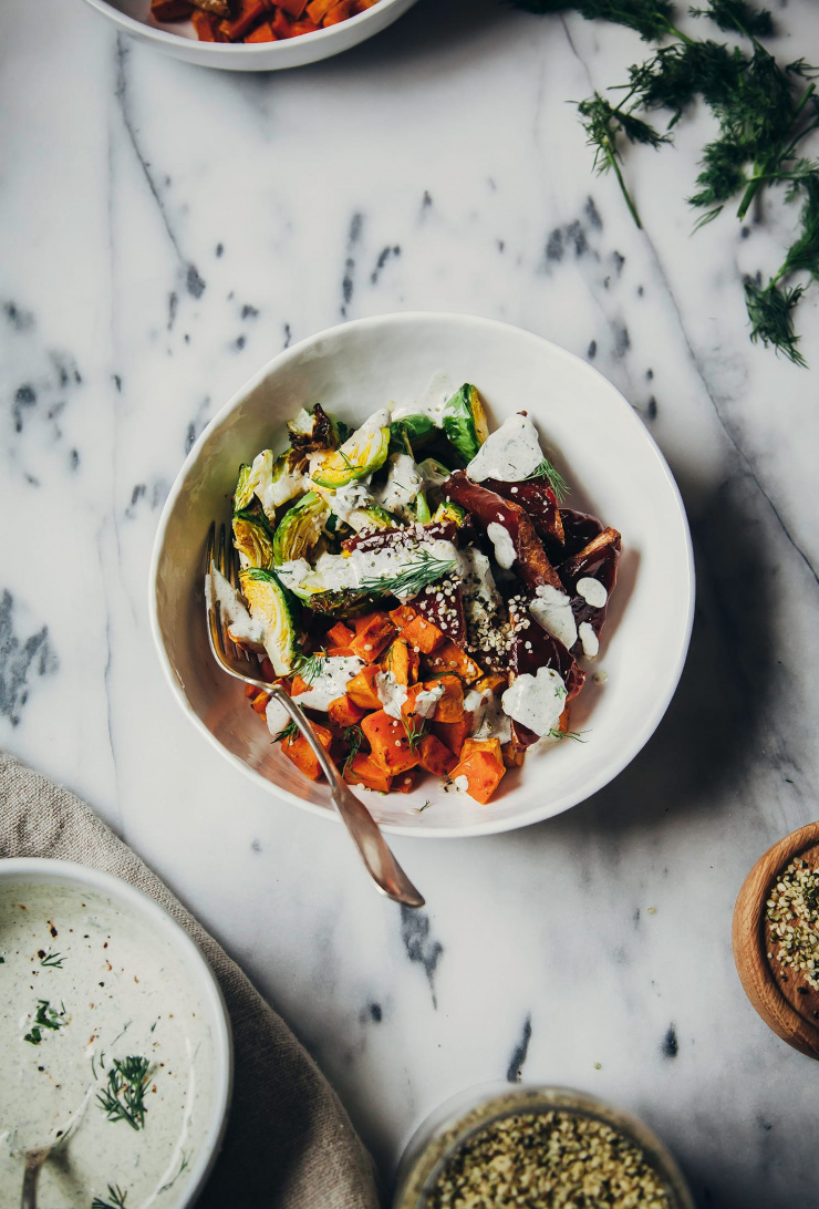 An overhead shot of a roasted winter bowl with sweet potatoes, saucy tempeh, brussels sprouts and a creamy sauce drizzled over the top.