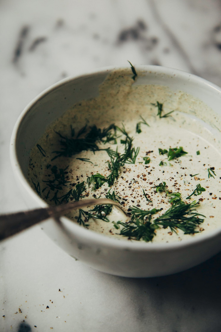 A 3/4 angle shot of a bowl of creamy sauce topped with ground black pepper and chopped dill.