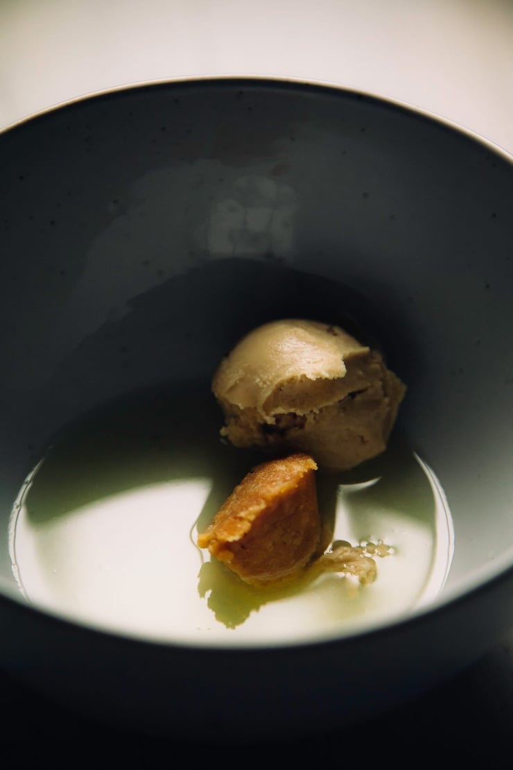 Image shows a dollop of tahini and miso in a bowl of liquid in dark, shadow-y lighting.