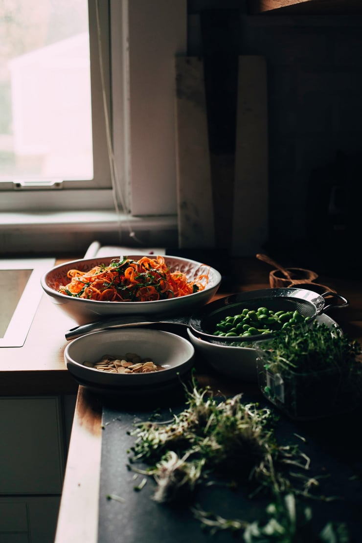 A 3/4 angle shot of ingredients for a salad on a kitchen counter with a window in the background. The lighting is moody and dark.