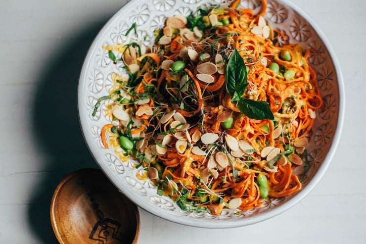 An overhead shot of orange sweet potato noodles topped with herbs, green edamames, sliced almonds, and sprouts.