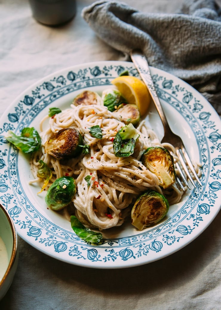 A 3/4 angle shot of creamy miso pasta with Brussels sprouts. The plate is white with a blue detail around the edge.
