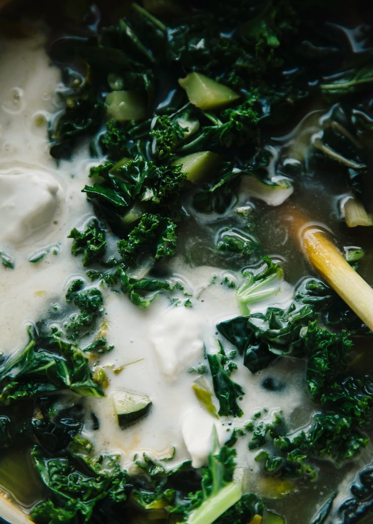 An up close shot of kale wilting in a pot of soup with a big puddle of creamy coconut milk in the middle.