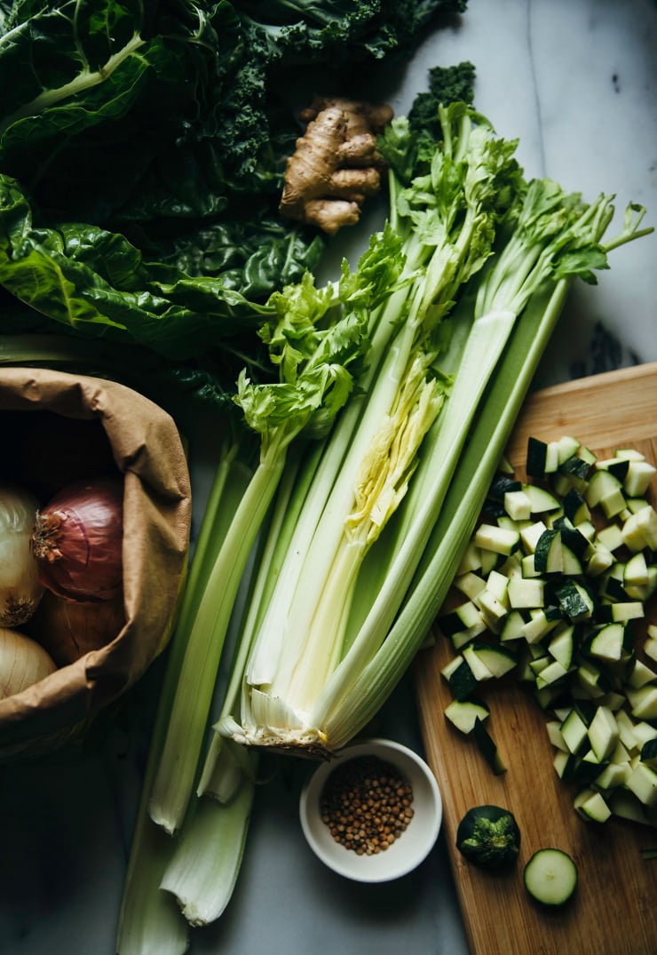 Overhead shot of ingredients for soup on a white marble background and bamboo cutting board.
