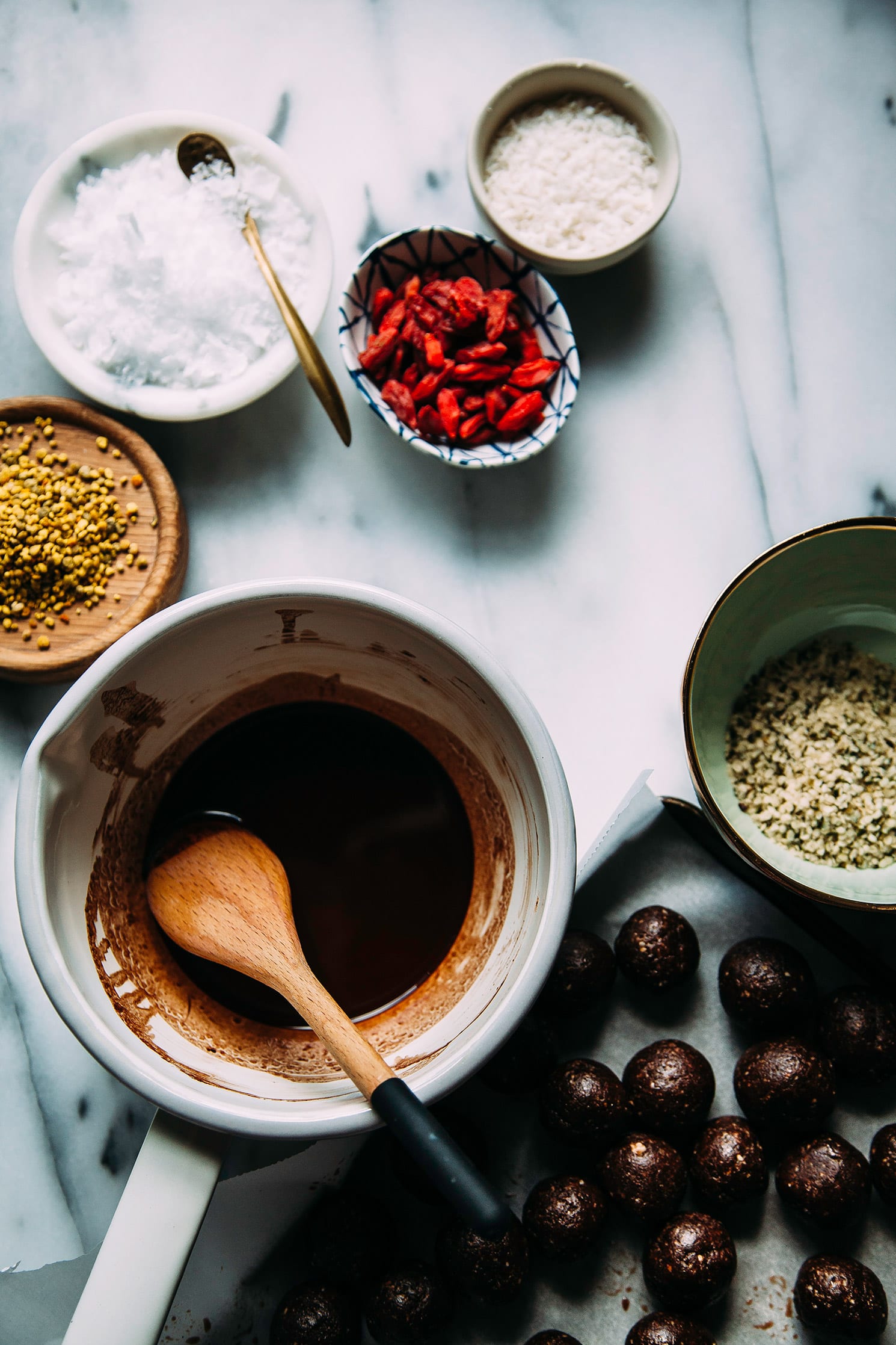 An overhead shot shows rolled up bites, melted chocolate, and garnishes on a marble background.