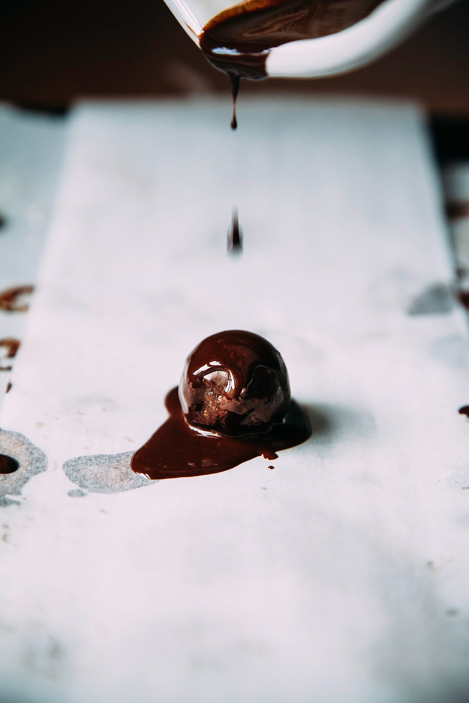 A head on shot shows melted chocolate being poured onto an individual superfood brownie bite.