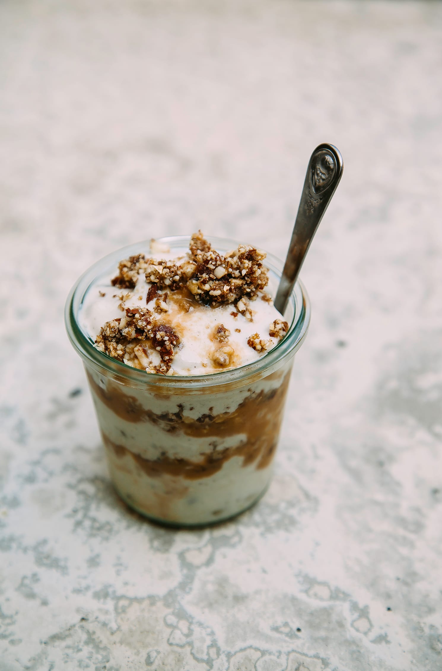 A 3/4 angle shot of a vegan peanut caramel sundae layered in a glass jar.