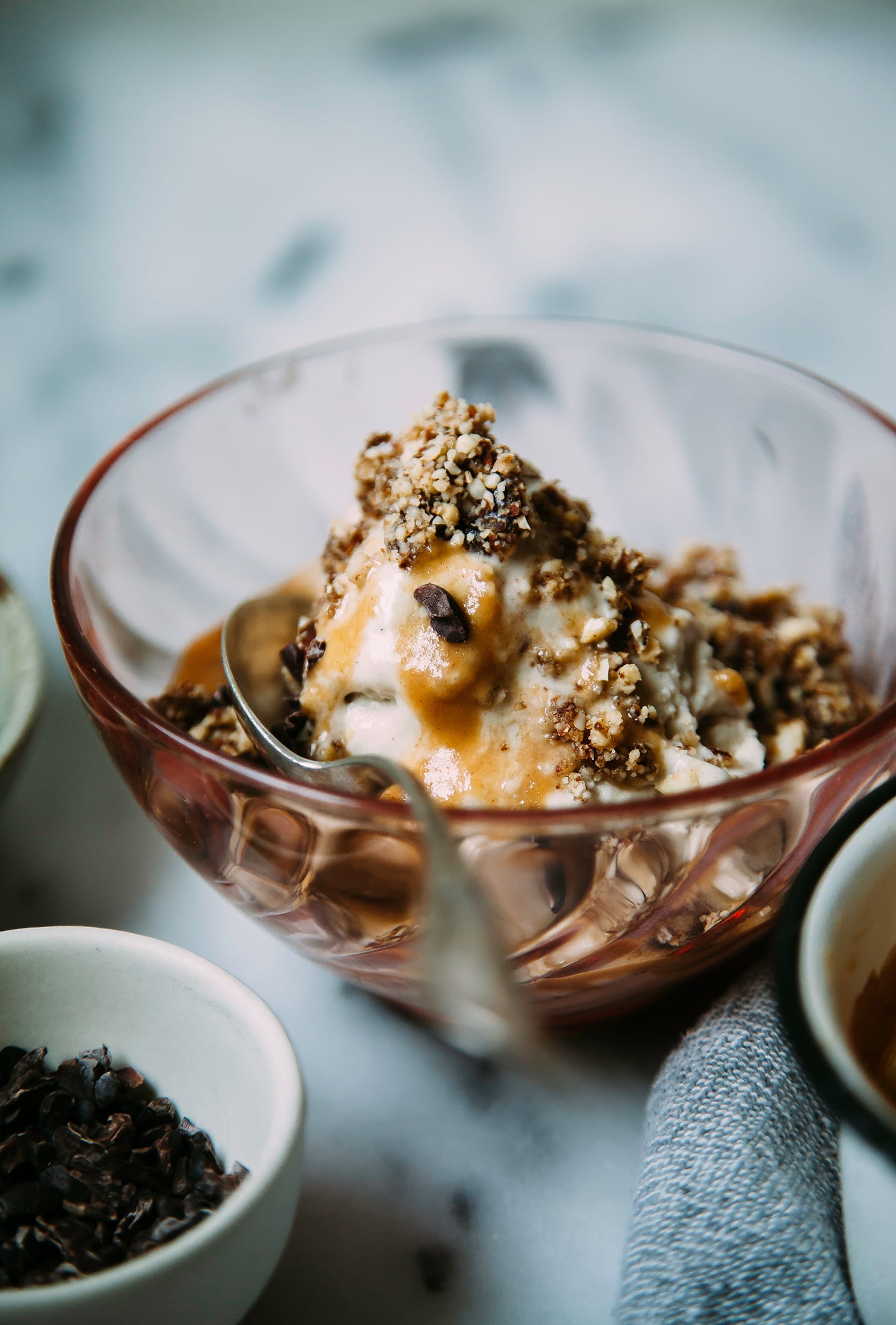 A head-on shot of a vegan peanut caramel sundae with vanilla cake crumble on top in a pink glass bowl.