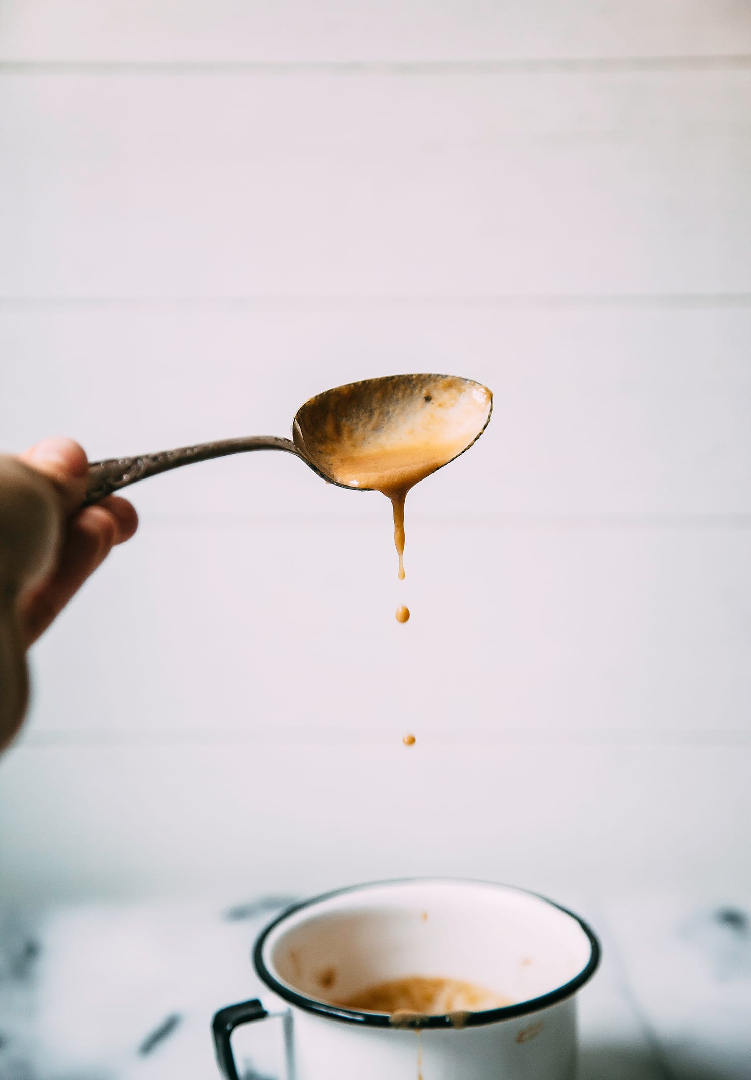 Image shows a hand holding a spoon that is dripping with a peanut butter caramel sauce.