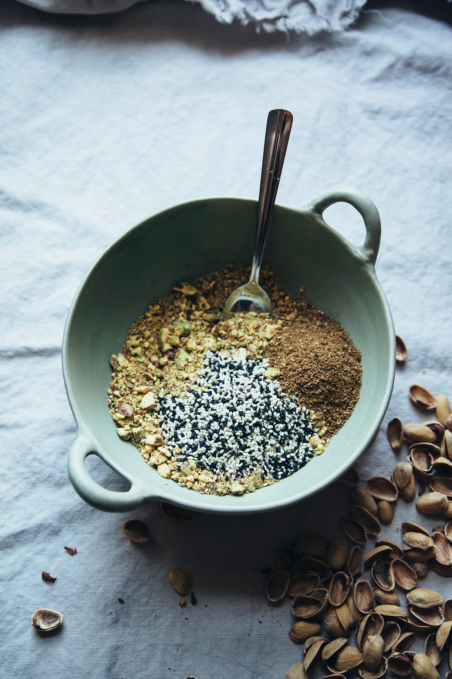 An overhead shot of pistachio dukkah ingredients in a light green bowl, pre-mixing.