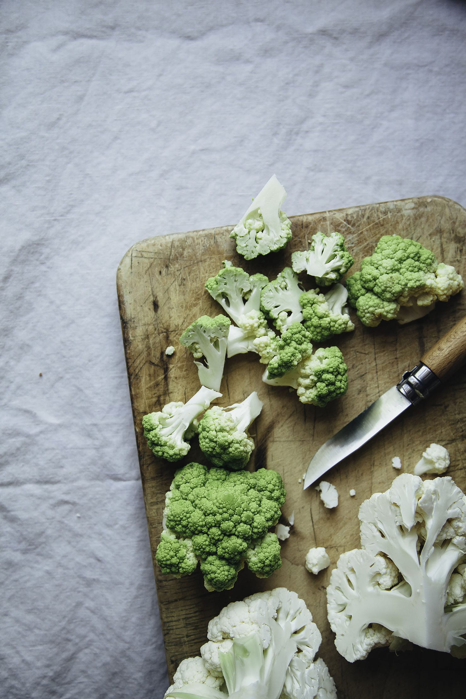 An overhead shot of cauliflower being sliced on a wood cutting board.