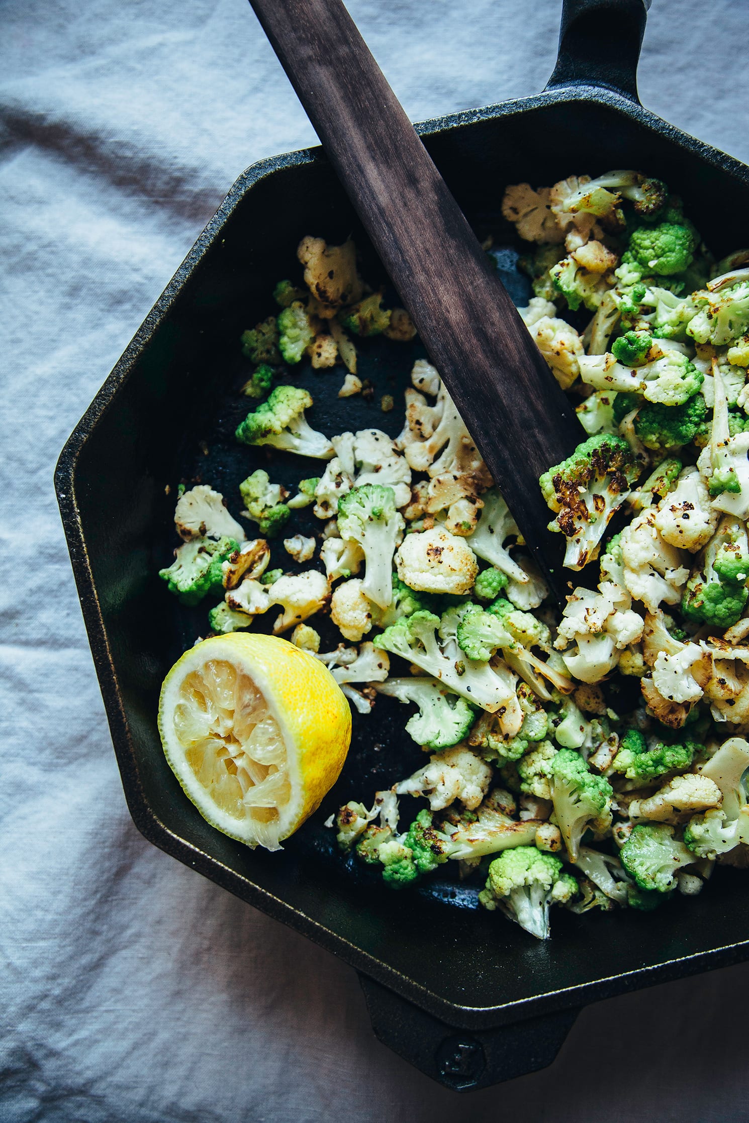 An overhead shot of cauliflower being sautéed in a cast iron skillet. A half of lemon is also seen inside the skillet.