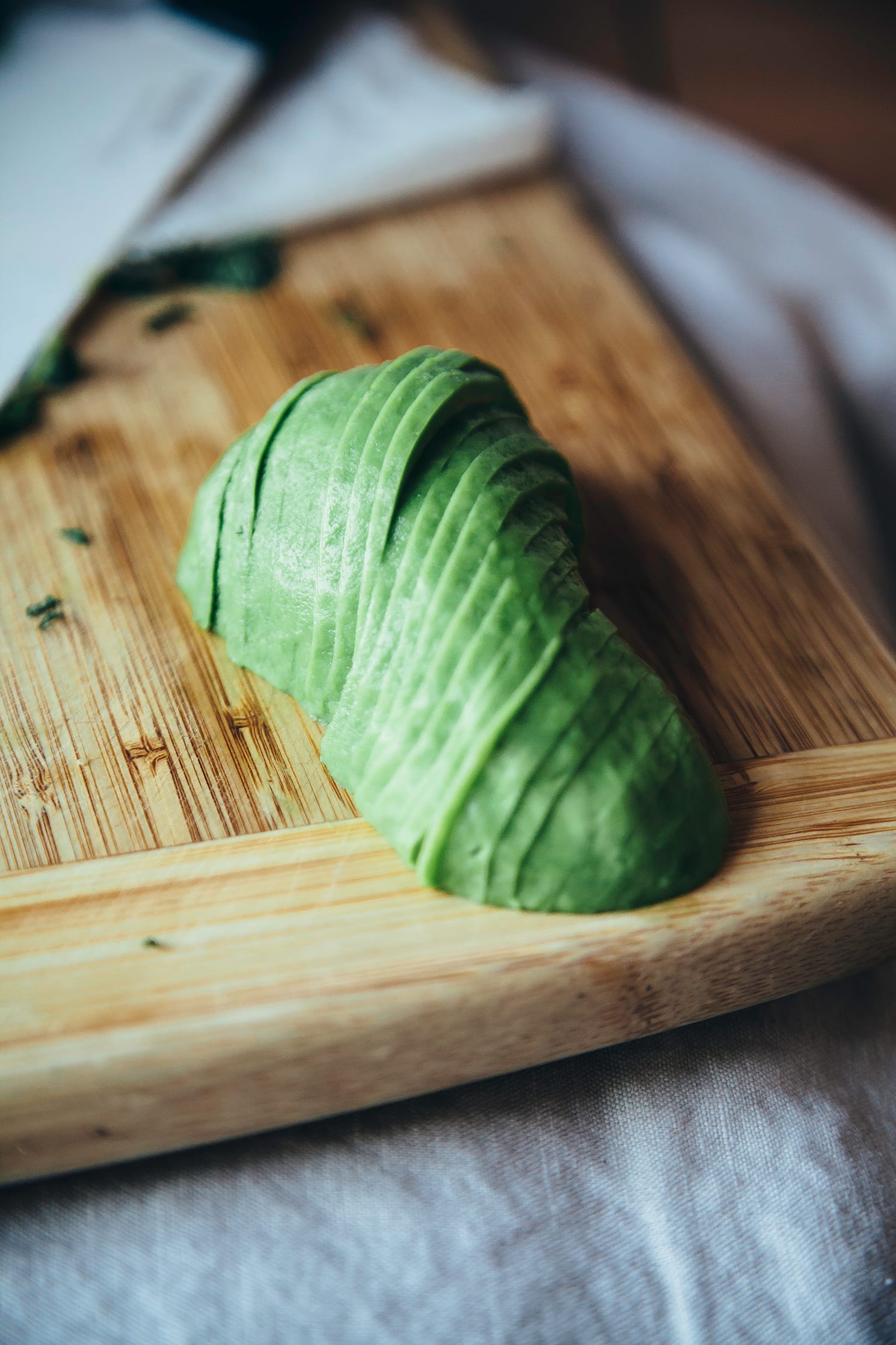 A 3/4 angle image of a thinly sliced avocado on a wood cutting board.