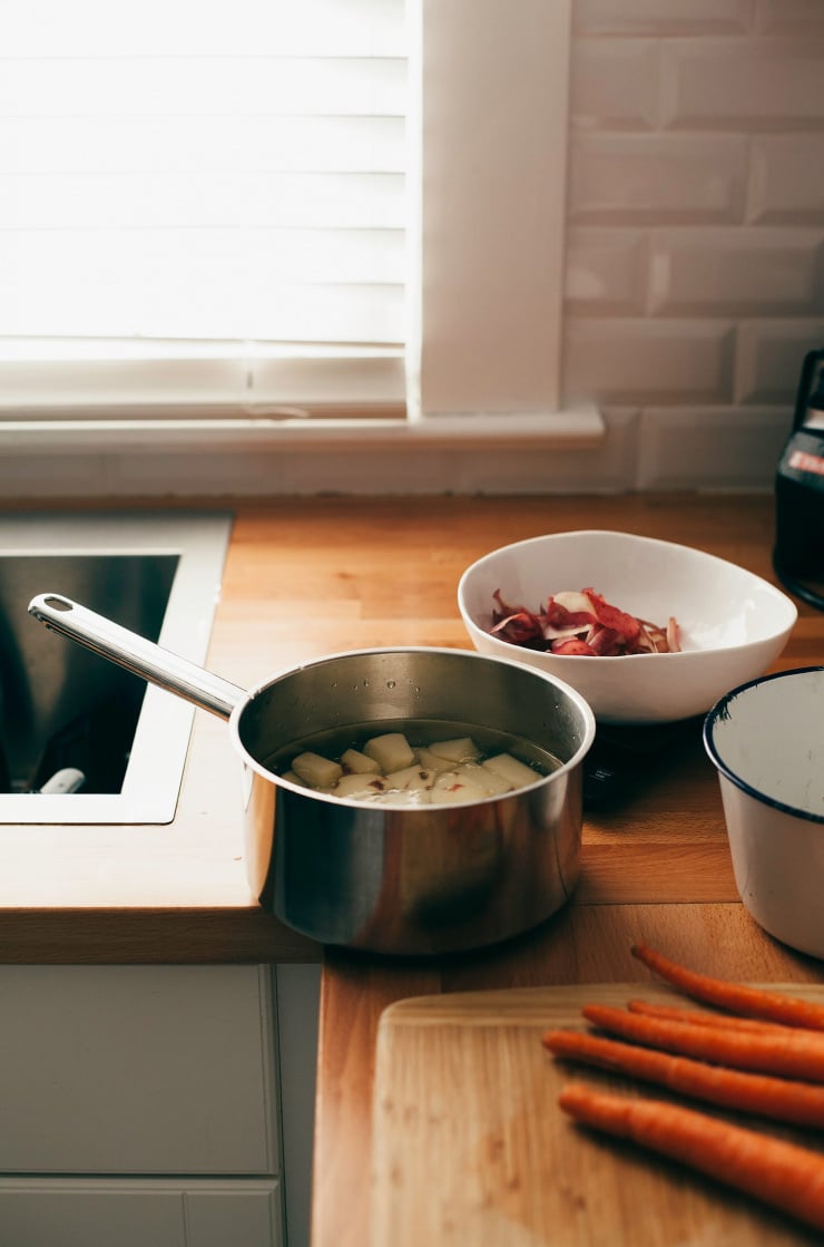 A 3/4 angle shot of a kitchen scene with a pot of cooked potatoes on the counter next to a bowl of kitchen scraps.