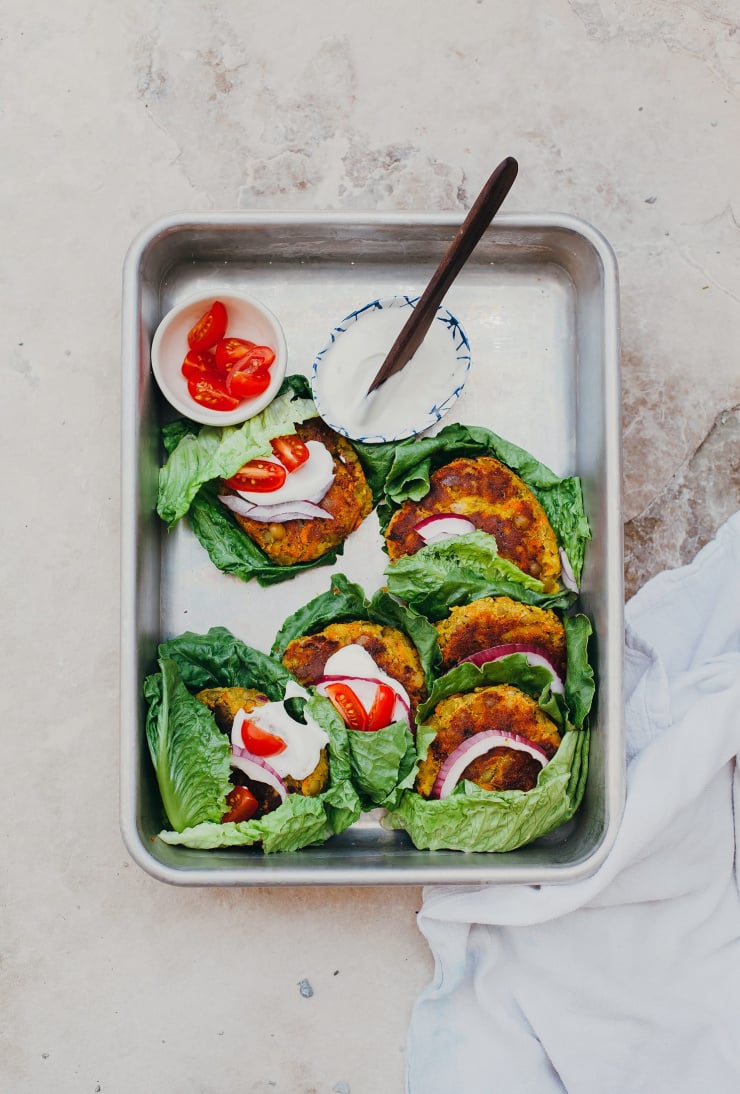 An overhead shot of a metal tray filled with lettuce-wrapped golden split pea patties.