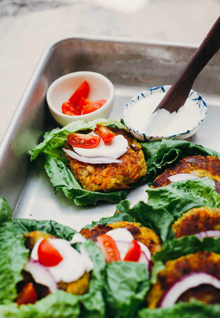 A 3/4 angle shot of a metal tray filled with lettuce-wrapped golden split pea patties.