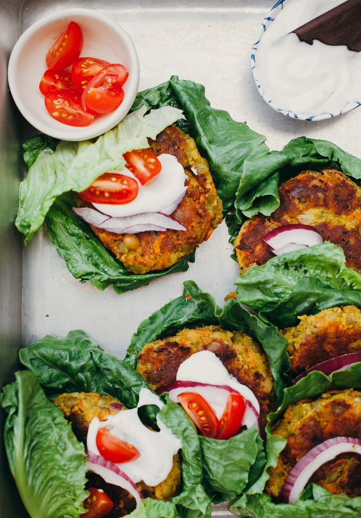 An overhead shot of a metal tray filled with lettuce-wrapped golden split pea patties.