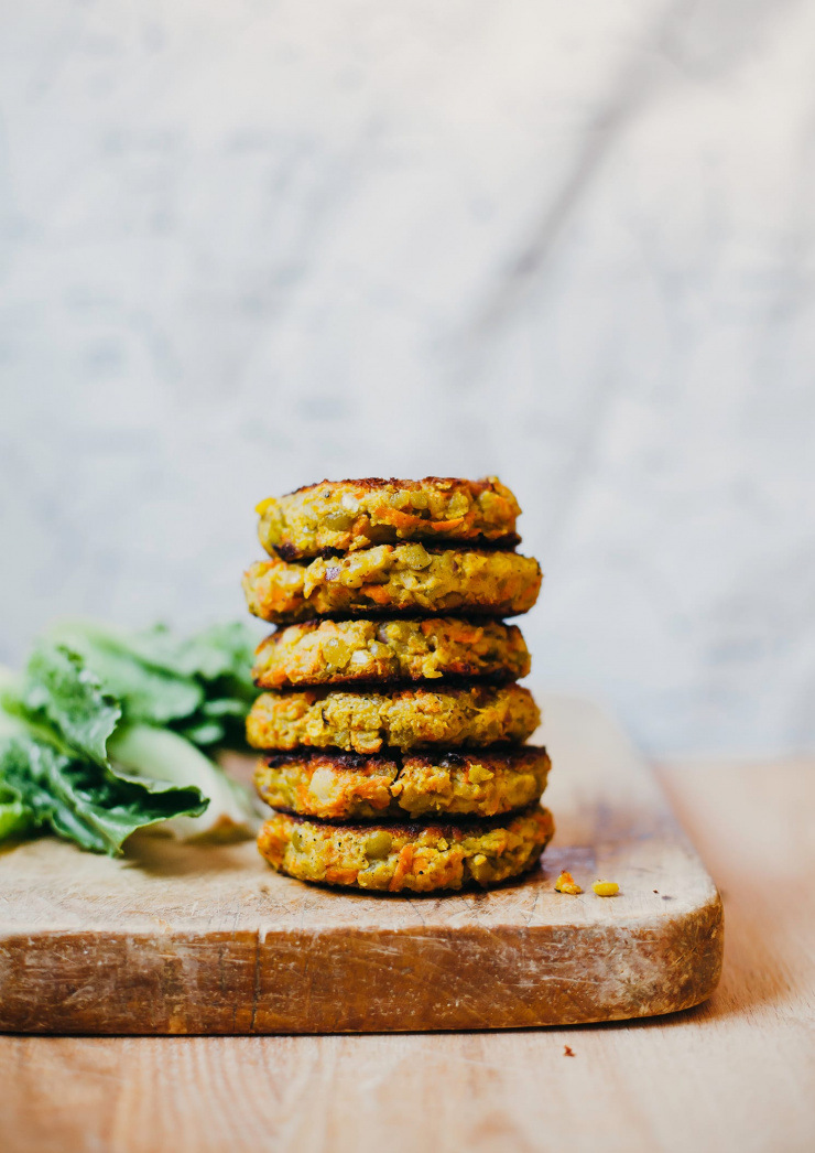 A head-on shot of 6 golden split pea patties stacked on top of each other on a wood cutting board.