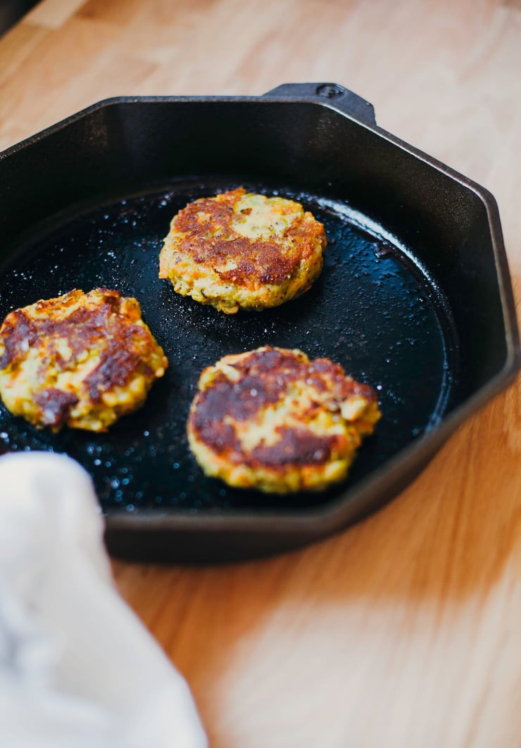 A 3/4 angle shot of veggie patties cooking in a cast iron pan.