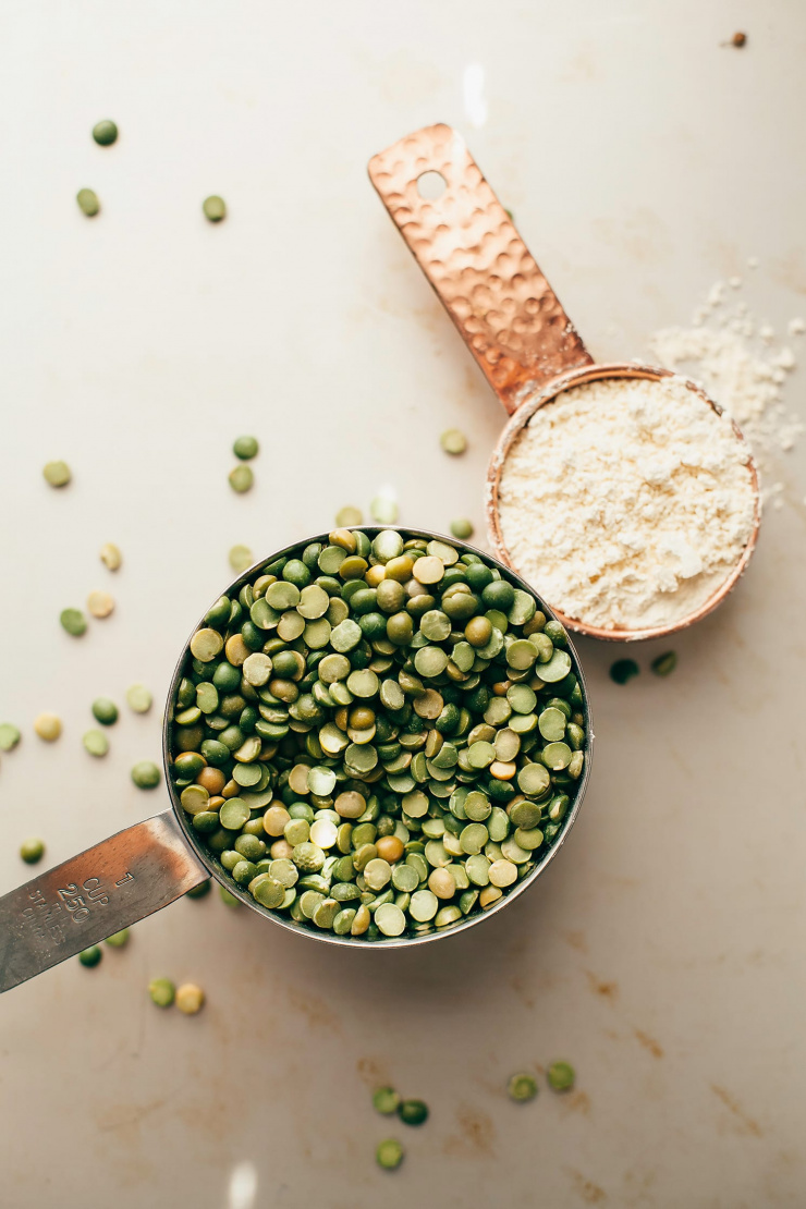 An overhead shot of two measuring cups containing dry split peas and chickpea flour.