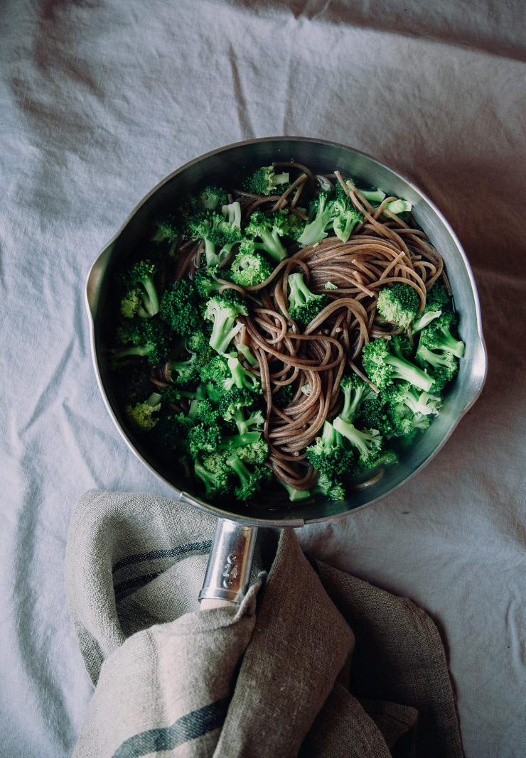 An overhead shot of broccoli and noodles being cooked in the same saucepan.