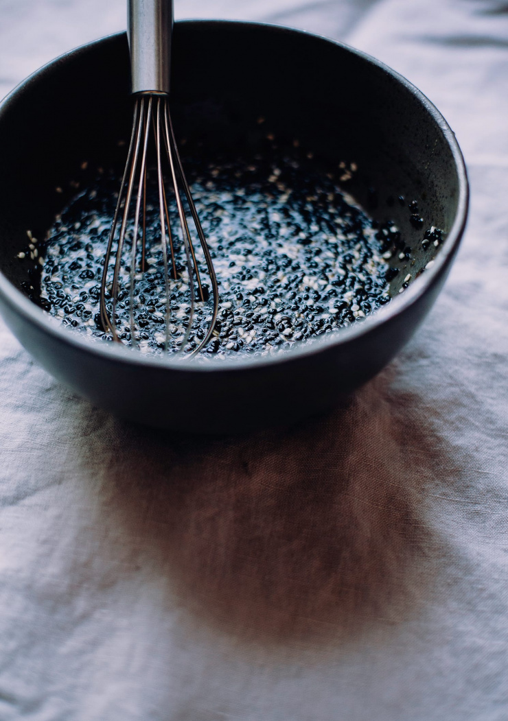 A 3/4 angle shot of a garlic sesame sauce being whisked up on a black bowl.