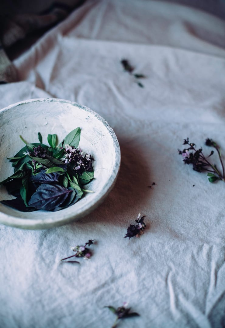 A 3/4 angle shot of some leaves of basil in a stoneware bowl.