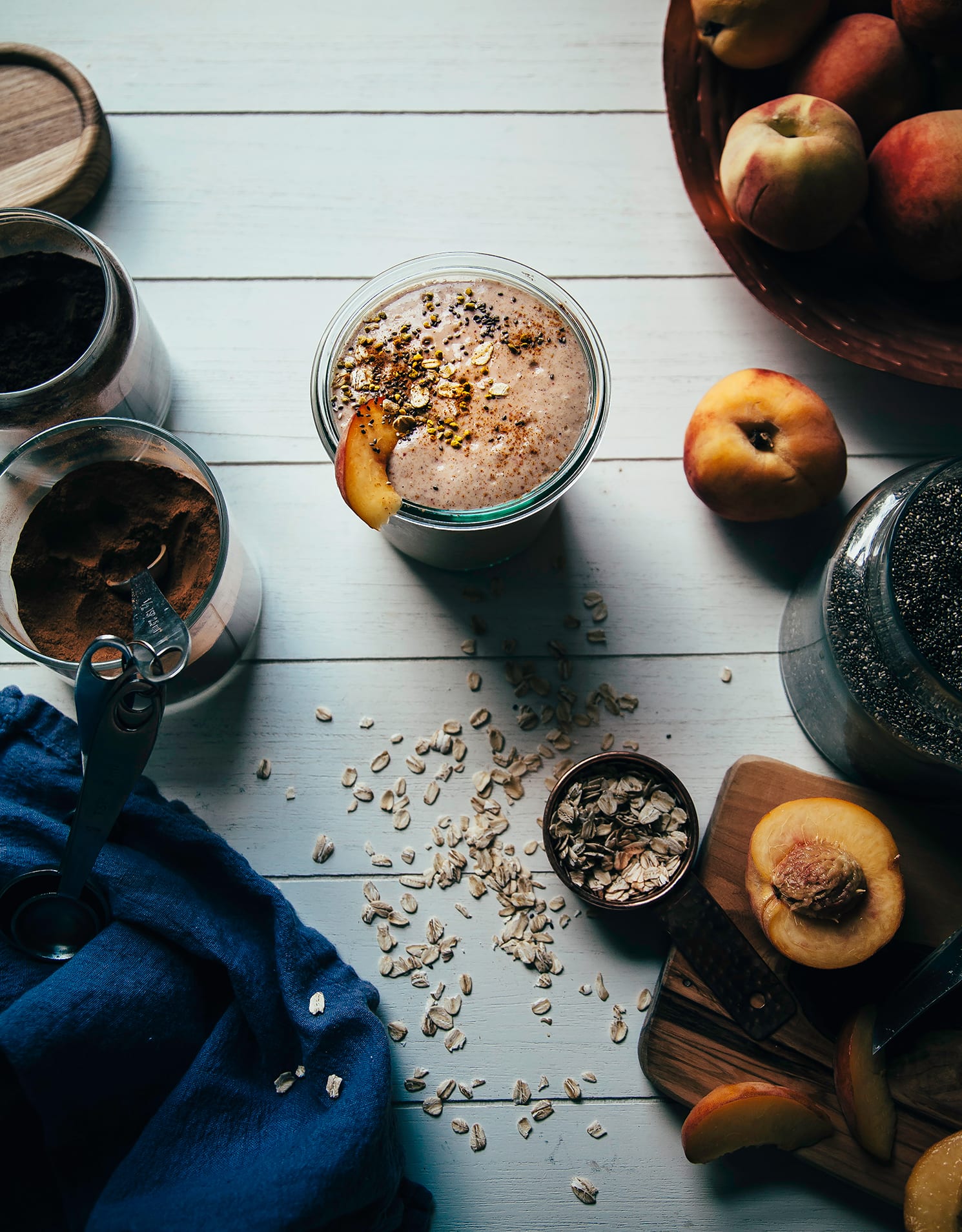 Overhead shot of a peach crumble shake on a white wood background with ingredients to the side.