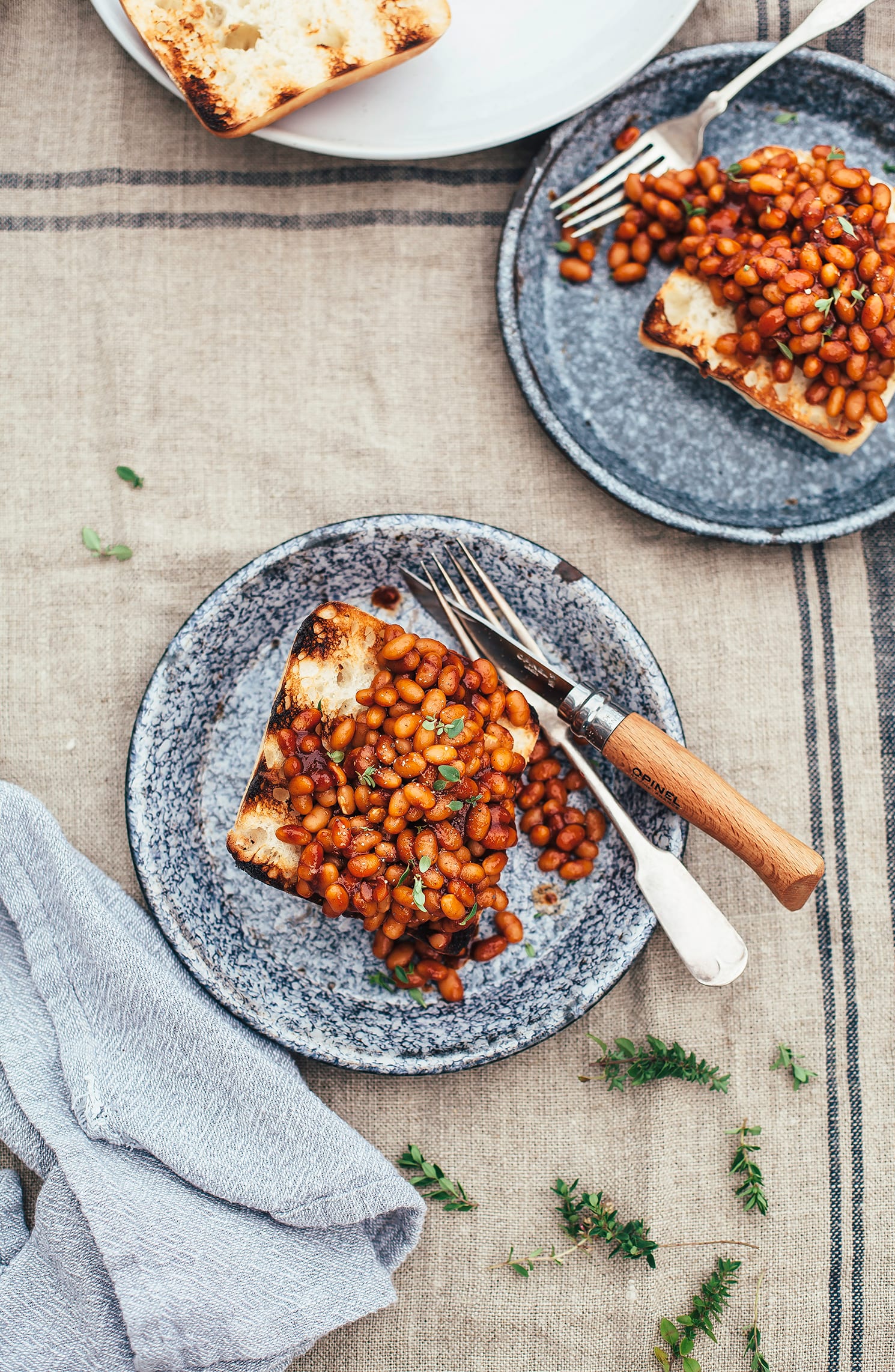 n overhead shot of some saucy and brown baked beans piled onto a grilled piece of ciabatta, all on top of a blue enamelware plate.