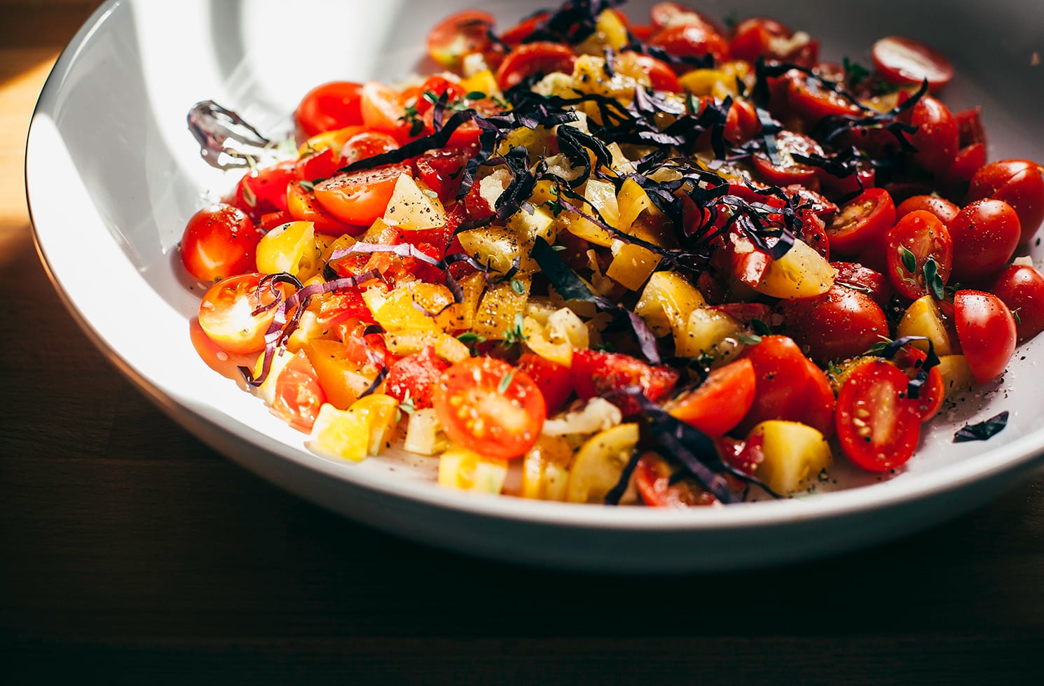 A 3/4 angle shot of a bowl of chopped, different coloured tomatoes.