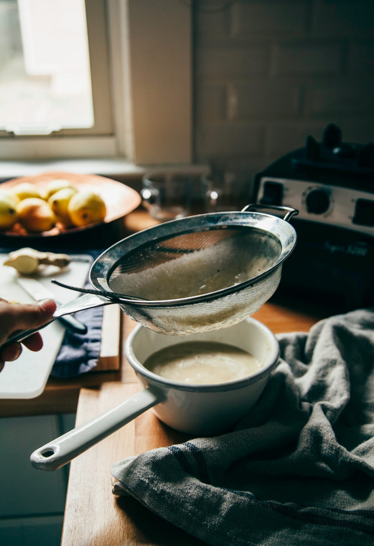 Image shows a strainer over a small saucepan with a beige liquid in the saucepan.