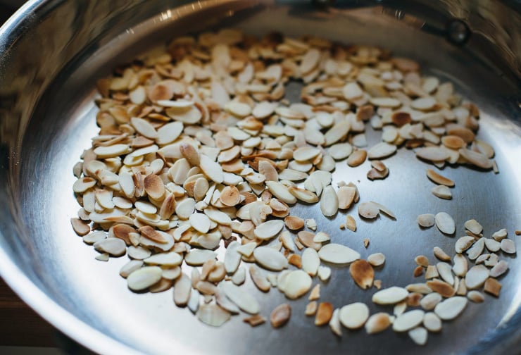 An up close shot of sliced almonds toasting in a pan.