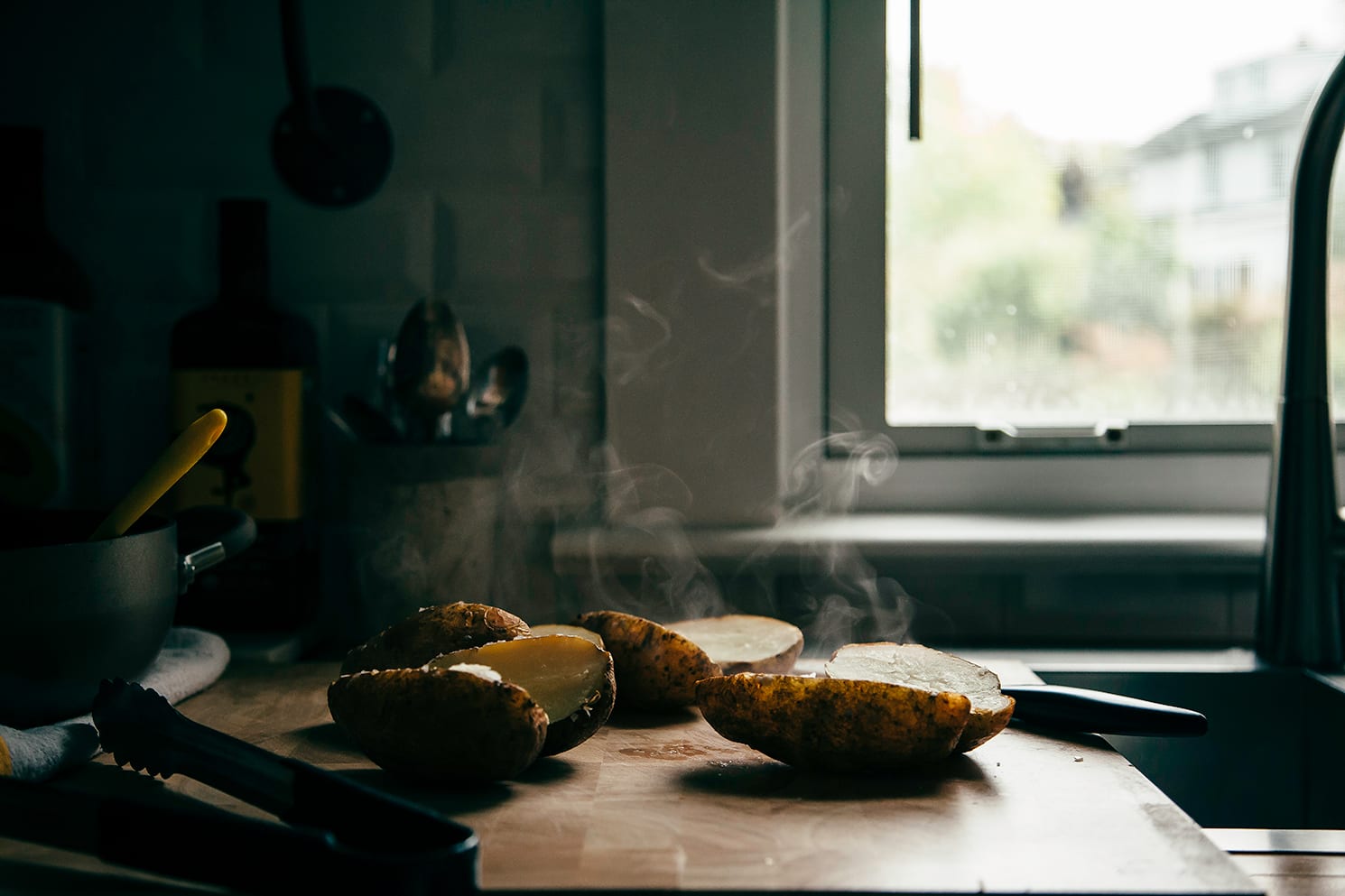 Image shows steaming, split open baked potatoes on a cutting board.