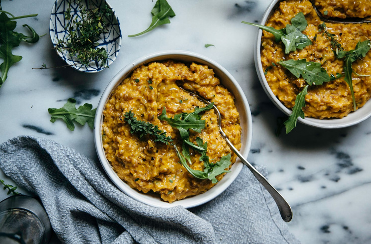 An overhead shot of an orange-hued vegan butternut farrotto dish in an individual serving bowl.