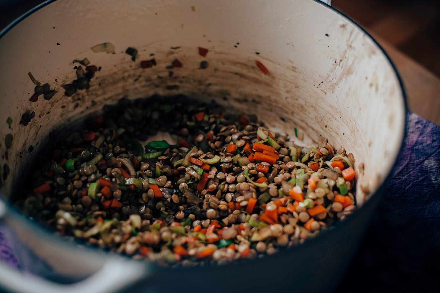 Image shows vegetables and lentils sautéing in a Dutch oven-style pot.