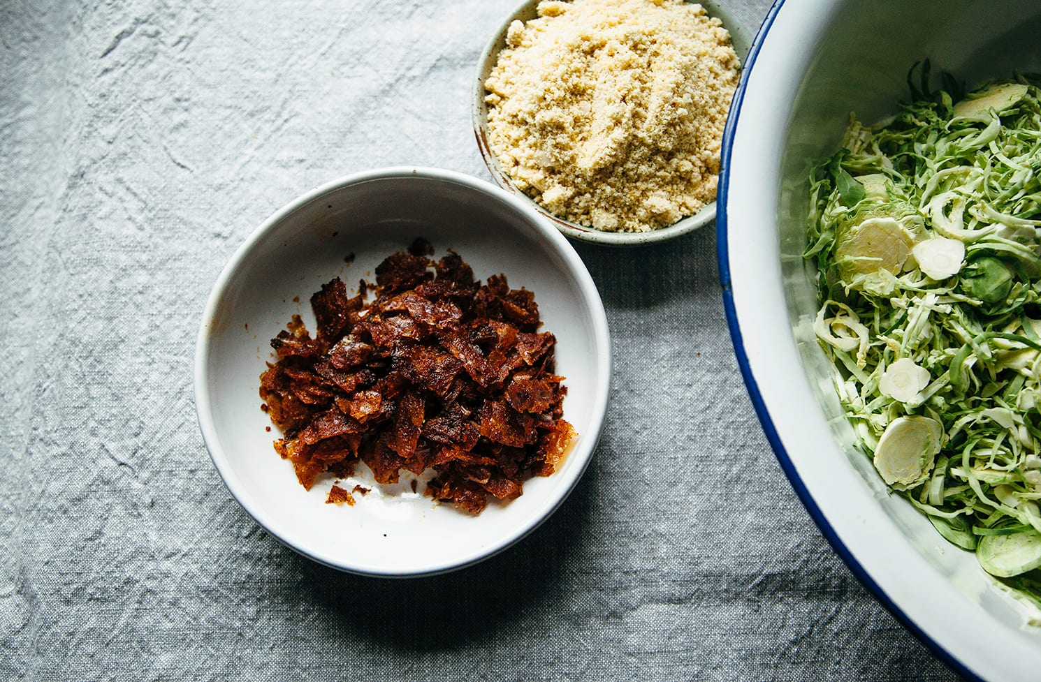 An overhead shot of prepped components for a brussels sprout salad in 3 separate bowls.