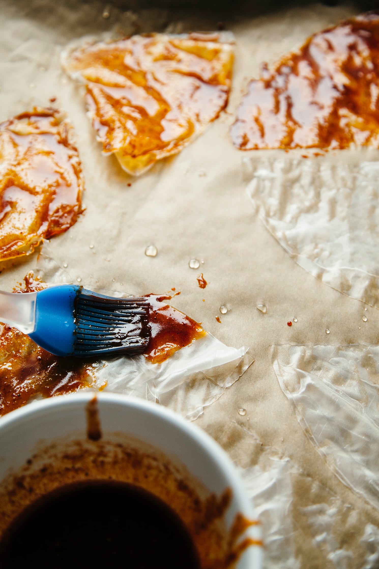 Image shows a deep red liquid being brushed onto pieces of soaked rice paper wrappers.