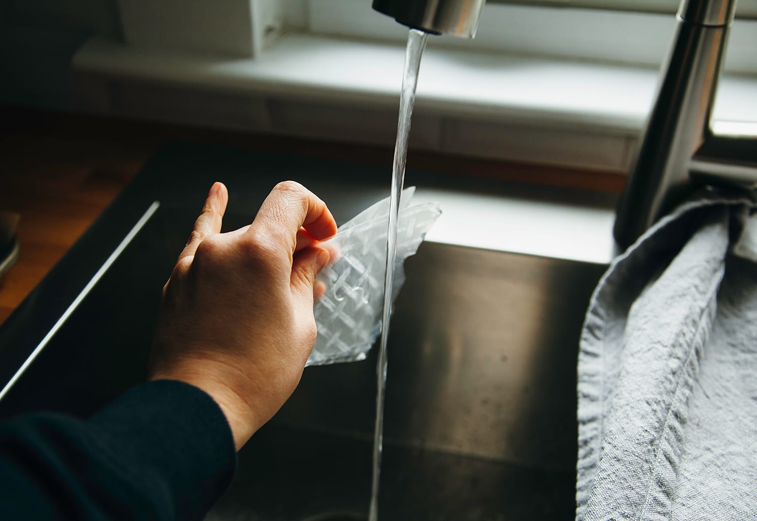 Image shows a hand running rice paper wrappers under water in a kitchen sink.