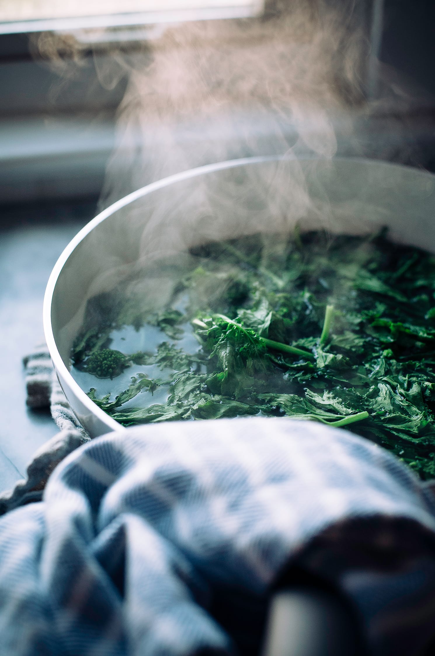 A 3/4 angle shot shows chopped broccoli rabe simmering and steaming in a skillet with some water.