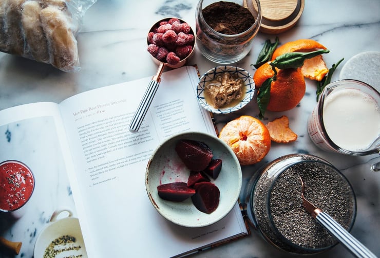 An overhead shot of ingredients for a hot pink beet smoothie with The First Mess Cookbook open to the recipe. Everything is on a white marble background.