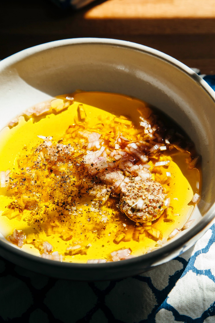 A 3/4 angle image of ingredients for a shallot salad dressing in a white bowl, pre-whisking.