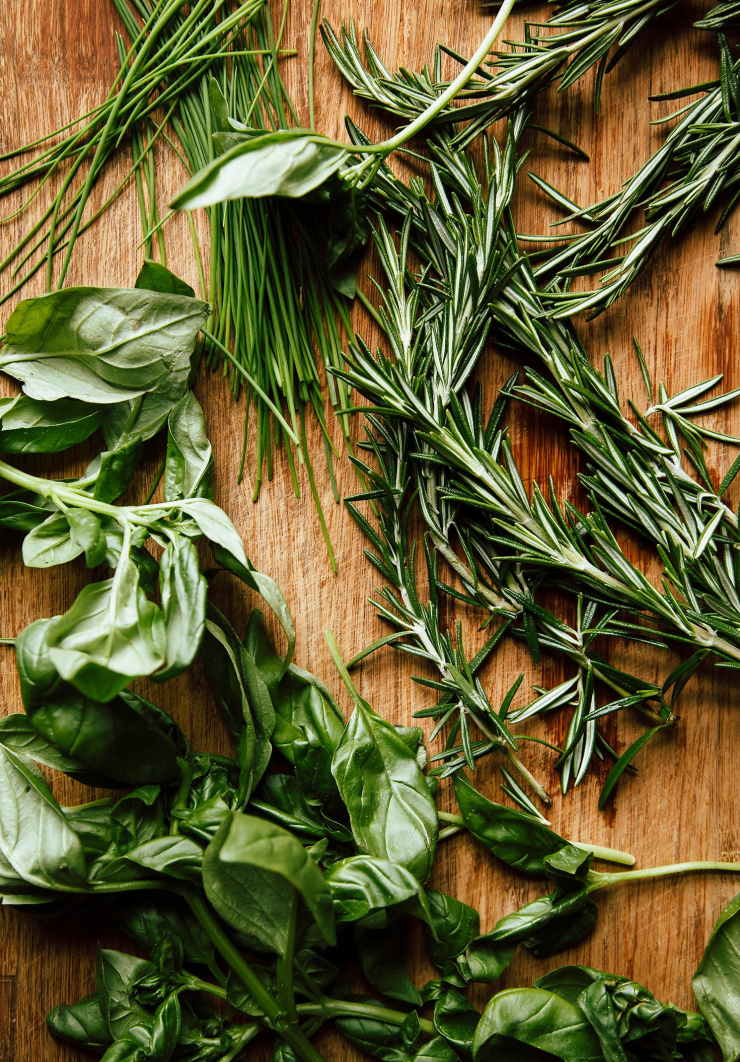 An overhead shot of some whole herbs on a cutting board (basil, chives and rosemary).