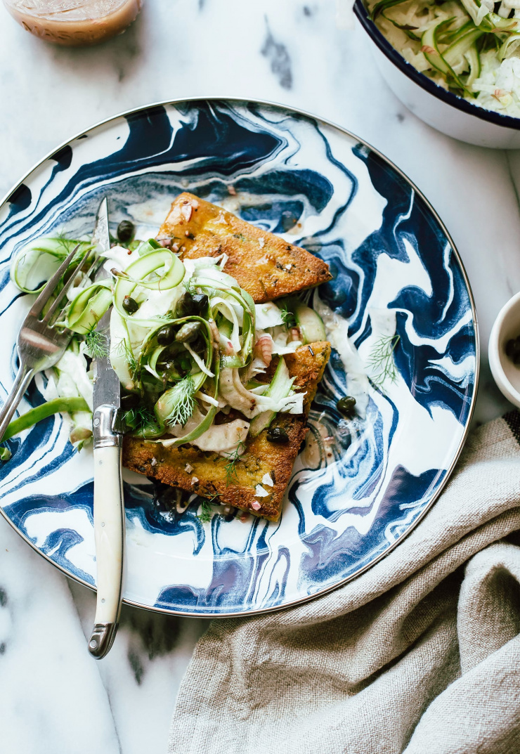 An overhead shot of two seared triangles of polenta on a marbled blue and white plate. The polenta is topped with a shaved vegetable salad.