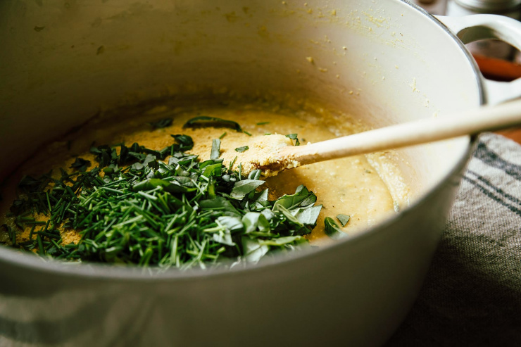 Image shows a pot of cooked polenta with a bunch of chopped herbs on top.
