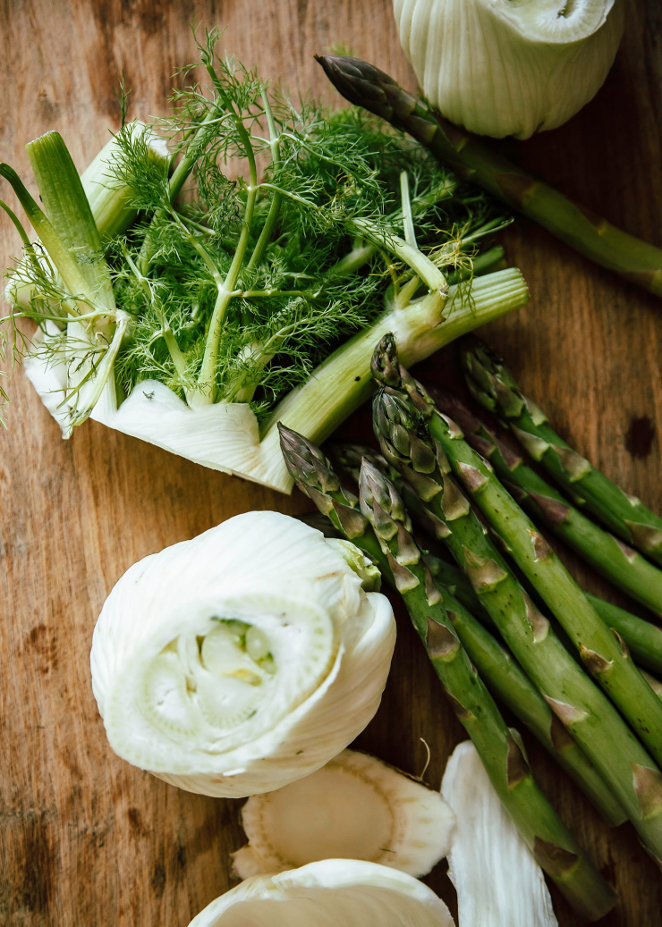 An overhead image of chopped fennel and whole asparagus on a wooden cutting board.
