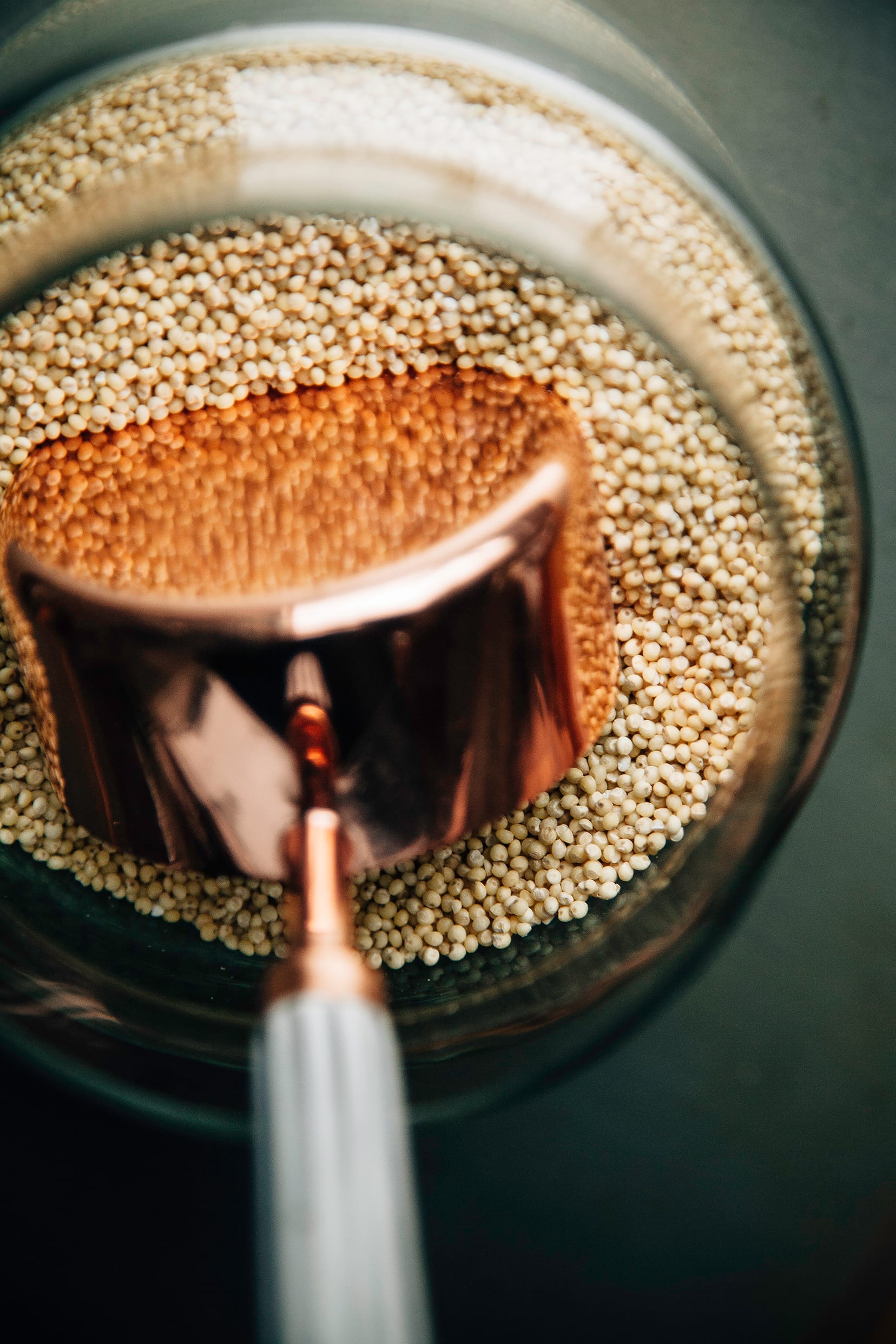 An up close overhead image of a bronze measuring cup inside a jar of dry millet.