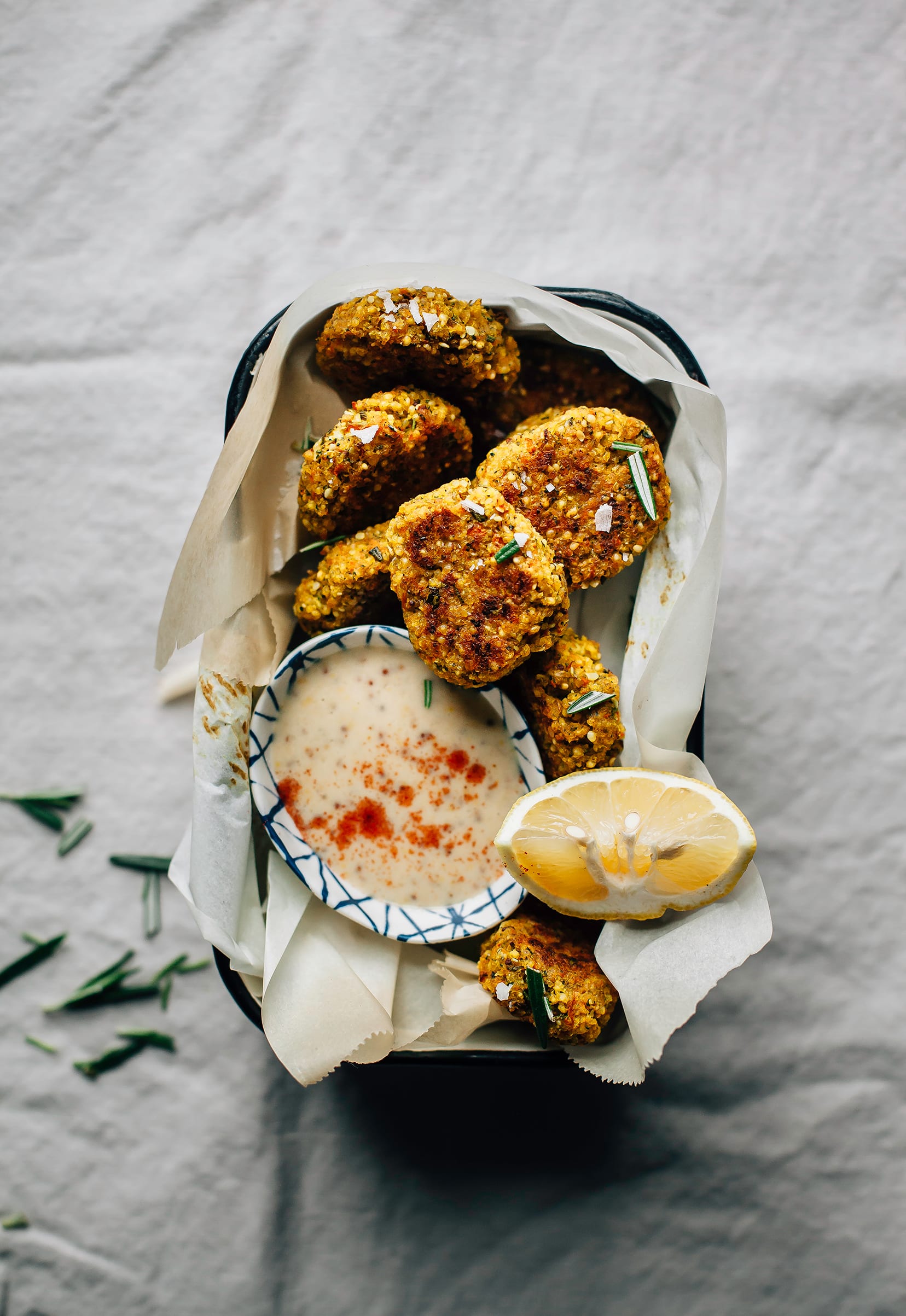 An overhead shot of a dish with golden brown veggie nuggets and a small bowl with a creamy dip. There is also a lemon wedge perched on the side.
